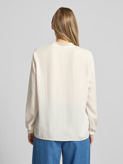 Frauenmodel trägt Bluse mit V-Ausschnitt und Label-Detail von Marc Cain in Creme, locker geschnitten, elastische Ärmelabschlüsse, Ganzkörperansicht Rückansicht.