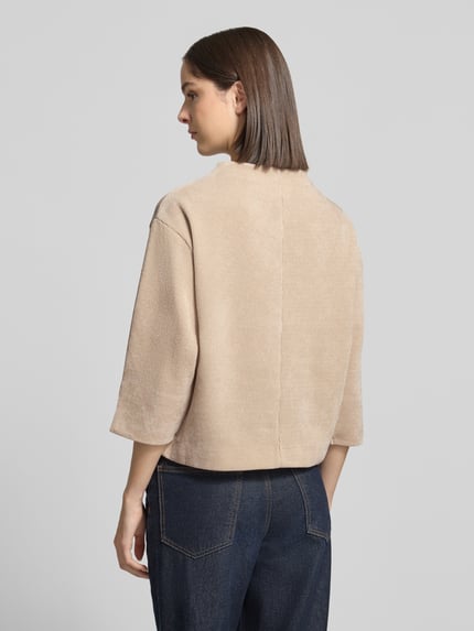 Frauenmodel trägt Relaxed Fit Strickpullover mit Stehkragen von ZABAIONE in Beige, Strick-Optik, 3/4-Arm, Rückansicht, Ganzkörperansicht.