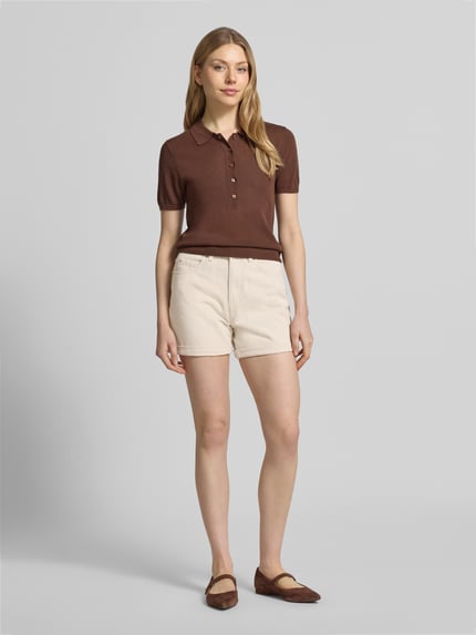 Frauenmodel trägt Loose Fit Jeansshorts aus Baumwoll-Mix Modell 'ZURI' von Vero Moda in heller Denim-Optik mit Label-Patch, 5-Pocket-Design, fixiertem Beinabschluss, Knopf und verdecktem Reißverschluss, Twill-Materialverarbeitung, Ganzkörperansicht von vorne.