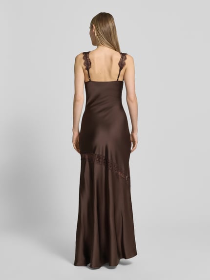 Frauenmodel trägt Maxikleid mit Spitzenbesatz und Gehschlitz von Little Mistress in Braun, figurbetont, Material-Mix mit Stretch-Anteil, Ganzkörperansicht Rückansicht.