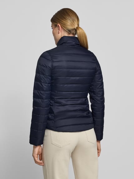 Frauenmodel trägt Slim Fit Steppjacke mit Logo-Detail von Lacoste, dunkelblauer Stoff, gesteppte Struktur, Ganzkörperansicht Rückansicht, Damen Steppjacke von Lacoste.