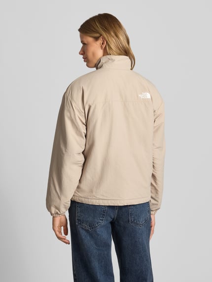 Frauenmodel trägt Jacke mit Wendefunktion Modell 'YUMIORI' von The North Face in Beige, leicht strukturierte Oberfläche, Jeans, Ganzkörperansicht Rückansicht. Rückenlänge 62 cm, Schulterbreite 52 cm, Brustweite 57 cm, Ärmellänge 57 cm, Regular Fit, Stehkragen, Logo, Damen Jacke.