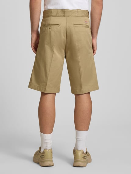 Männermodel trägt Bermudas mit französischen Eingrifftaschen von Dickies aus Reine Baumwolle in Beige, Straight Fit, Knopf-Reißverschluss, Bundweite 42 cm, Innenbeinlänge 31 cm, Gesäßtaschen, Ganzkörperansicht Rückansicht.