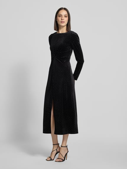 Frauenmodel trägt Cocktailkleid im Allover-Look Modell 'HELLA' von YAS, figurbetont, schwarzer Stoff mit weißen Punkten, Ganzkörperansicht von vorne.