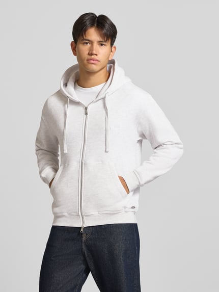 Männermodel trägt Relaxed Fit Sweatjacke aus Baumwoll-Mix Modell 'ORSALAMANCO' von JACK & JONES in Hellgrau, Struktur glatt, Ganzkörperansicht von vorne. Herren Sweatjacke, Kapuze mit Tunnelzug, Känguru-Tasche, Zweiwege-Reißverschluss, elastische Abschlüsse, Rückenlänge 69 cm, Ärmellänge 63 cm.