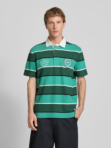 Männermodel trägt Regular Fit Poloshirt aus reiner Baumwolle von Tommy Jeans in Two-Tone-Optik mit Label-Print, Motiv-Print, Jersey-Textur, Ganzkörperansicht von vorne.