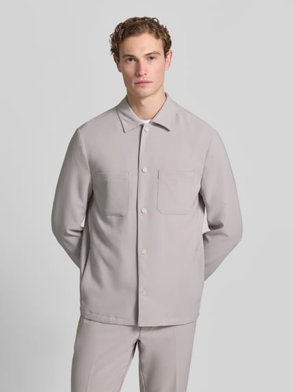 Männermodel trägt Regular Fit Overshirt mit Brusttaschen von MCNEAL in hellem Grau, Material-Mix mit Stretch-Anteil, Kentkragen, Druckknopfverschluss, Sportmanschetten, Rückenlänge bei Größe M: 73 cm, Ganzkörperansicht von vorne.