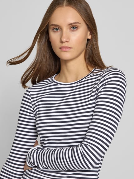 Frauenmodel trägt Slim Fit Langarmshirt mit Rundhalsausschnitt von REVIEW, elastischer Baumwoll-Mix, schwarz-weiß gestreift, Nahaufnahme Oberkörper.