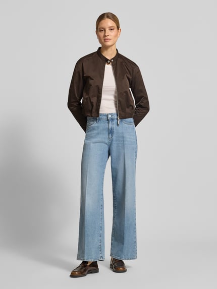 Frauenmodel trägt Cropped Jacke mit Zweiwege-Reißverschluss von monari in Dunkelbraun, kombiniert mit Jeans und weißem Shirt, Ganzkörperansicht von vorne. Rückenlänge 49 cm, Schulterbreite 50 cm, Brustweite 44 cm, Ärmellänge 56 cm.