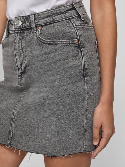 Frauenmodel trägt Regular Fit Jeansrock aus Baumwoll-Mix Modell 'TESSA' von Vero Moda in Denim-Optik, Mini-Länge, 5-Pocket-Design, Label-Patch, Knopf und verdeckter Reißverschluss, Twill-Materialverarbeitung, Nahaufnahme Oberkörper.