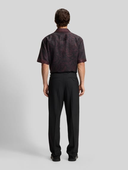 Mężczyzna nosi Regular Fit Anzughose mit Bügelfalten Modell 'FLIPS251X' od HUGO, czarny stretch-twill, kieszenie, widok całej sylwetki z tyłu.