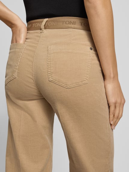 Frauenmodel trägt Regular Fit Cordhose mit seitlichen Eingrifftaschen Modell 'Jenny Wide' von TONI in Beige, sichtbare Struktur, Nahaufnahme Rückansicht, Cordmaterial, unifarben, sichtbare Gesäßtaschen, Gürtelschlaufen, Markenschriftzug am Bund.