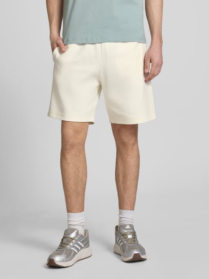 Männermodel trägt Shorts mit Label-Stitching mit elastischem Bund von CHAMPION in Beige, Baumwoll-Mix, Regular Fit, Ganzkörperansicht von vorne.