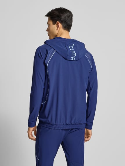 Mężczyzna nosi Regular Fit Kurtkę treningową z nadrukiem logo model 'Tech' od adidas Training, elastyczna mieszanka materiałów, kaptur z tunelem, elastyczne wykończenia, kieszeń kangurka, zamek błyskawiczny, długość tyłu 70 cm, długość rękawów 62 cm, widok całej sylwetki z tyłu.