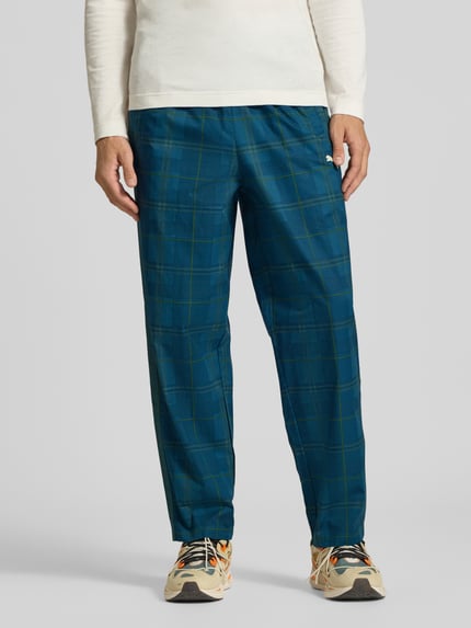 Männermodel trägt Relaxed Fit Trackpants aus reiner Baumwolle von PUMA im Tartan-Allover-Muster mit Logo-Stitching, Ganzkörperansicht von vorne.