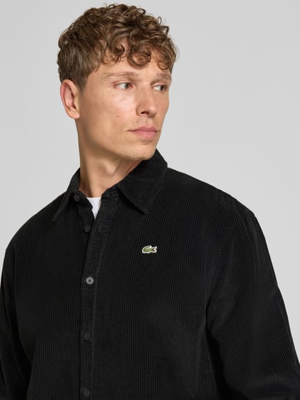 Männermodel trägt Regular Fit Cordhemd mit Logo-Applikation von LACOSTE in Schwarz, strukturierte Oberfläche, Nahaufnahme Oberkörper.