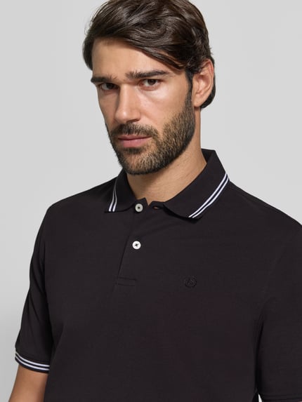 Männermodel trägt Slim Fit Poloshirt mit Label-Stitching von bugatti, reine Baumwolle, schwarzer Stoff, Nahaufnahme Oberkörper.