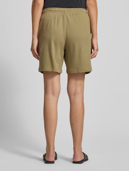 Frauenmodel trägt Shorts mit seitlichen Eingrifftaschen von Fynch-Hatton in Olivgrün, Loose-Fit, Label-Detail, Ganzkörperansicht Rückansicht. Bundweite bei Größe S: 41 cm, Innenbeinlänge bei Größe S: 20 cm, elastischer Bund mit Kordelzug.