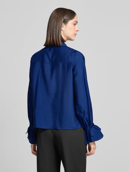 Frauenmodel trägt Bluse mit Volants und Bindung von monari in kräftigem Blau, Lyocell-Mix, Volantärmel, Rückenlänge 60 cm, Ganzkörperansicht Rückansicht.