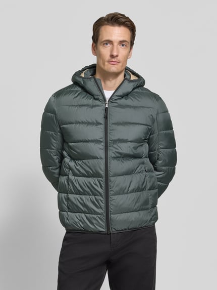 Männermodel trägt Steppjacke mit Kapuze und Reißverschluss von MCNEAL, Regular Fit, glatte Oberfläche, dezentes Grün, Ganzkörperansicht von vorne. Rückenlänge 70 cm, Schulterbreite 46 cm, Brustweite 54 cm, Ärmellänge 63 cm.