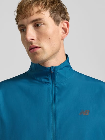 Männermodel trägt Trainingsjacke mit Stehkragen Modell 'FAST DAYS JACKET' von NEW BALANCE, unifarbenes Design, Logo-Print, Nahaufnahme Oberkörper