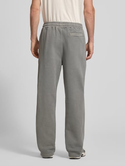 Männermodel trägt Loose Fit Sweatpants aus Baumwoll-Mix mit Label-Detail von PEGADOR in Grau, elastischer Bund, Eingrifftaschen, Ganzkörperansicht Rückansicht.
