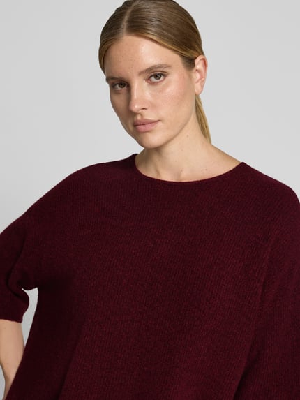 Frauenmodel trägt Oversized Strickpullover mit Leinen-Anteil von American Vintage in dunklem Rot, gerippter Rundhalsausschnitt, Nahaufnahme Oberkörper.