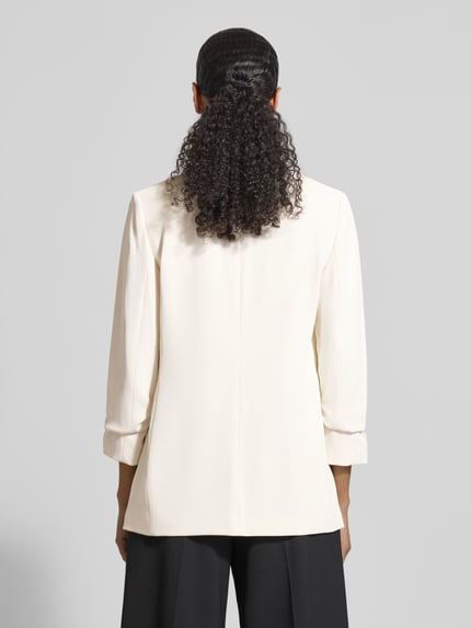 Männermodel trägt Blazer mit Pattentaschen von Jake*s Collection, kolor ecru, materiał z domieszką stretchu, krój luźny, widok całej sylwetki z tyłu. Długość pleców w rozmiarze 36: 69 cm, szerokość w rozmiarze 36: 44 cm, długość rękawa w rozmiarze 36: 52 cm.