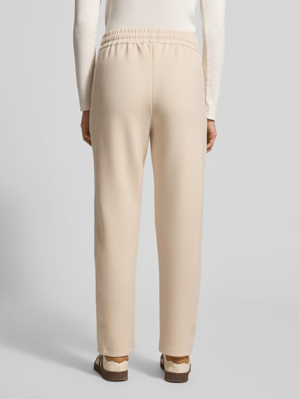 Vrouwenmodel draagt Sweatpants met elastische band Model 'Twinka' van JOOP! in beige, materiaalmix met modal, regular fit, labelstitching, tunnelkoord, volledig zicht van achteren.