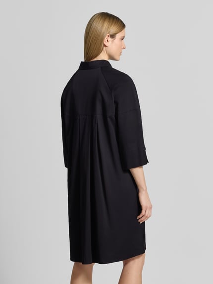 Frauenmodel trägt Hemdblusenkleid mit überschnittenen Schultern von Marc Cain, schwarze Farbe, Baumwoll-Kleid mit Viskose-Anteil, Gerader-Schnitt, 3/4-Arm, Hemdblusenkragen, verdeckte Knopfleiste, Label-Detail, Rückenlänge bei Größe 36: 101 cm, Brustweite: 53 cm, Ärmellänge: 48 cm, Ganzkörperansicht Rückansicht