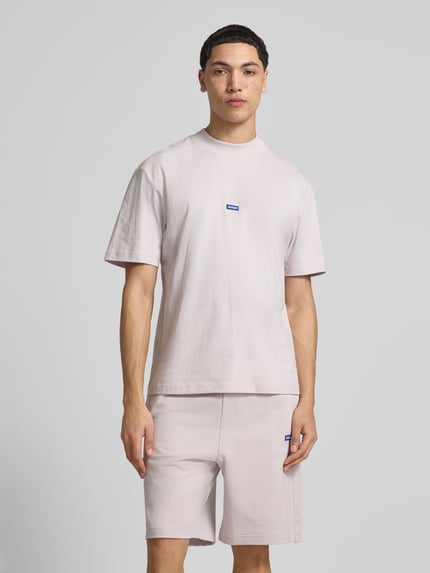 Męski model nosi Regular Fit T-Shirt aus reiner Baumwolle Modell 'Niereos' od HUGO Blue, jednolity jasnoróżowy dżersej, label patch, okrągły dekolt, krótki rękaw, Ganzkörperansicht von vorne.