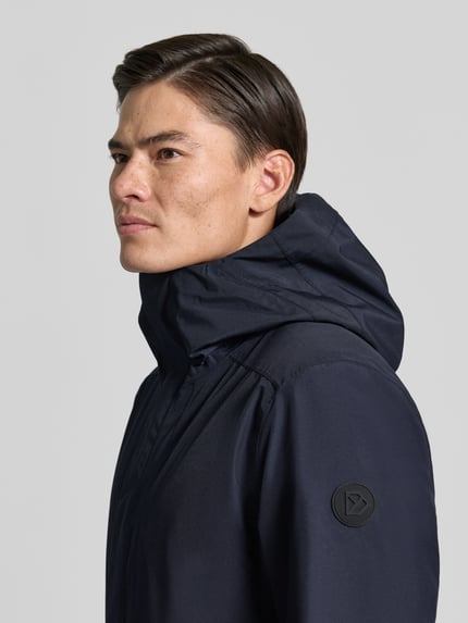 Männermodel trägt Regular Fit Parka mit Kapuze Modell 'Kenny' von Didriksons, dunkelblau, strukturierte Oberfläche, Nahaufnahme Oberkörper. Herren Parka, Eingrifftaschen, Rückenlänge 99 cm, Schulterbreite 48 cm, Brustweite 59 cm, Ärmellänge 72 cm.