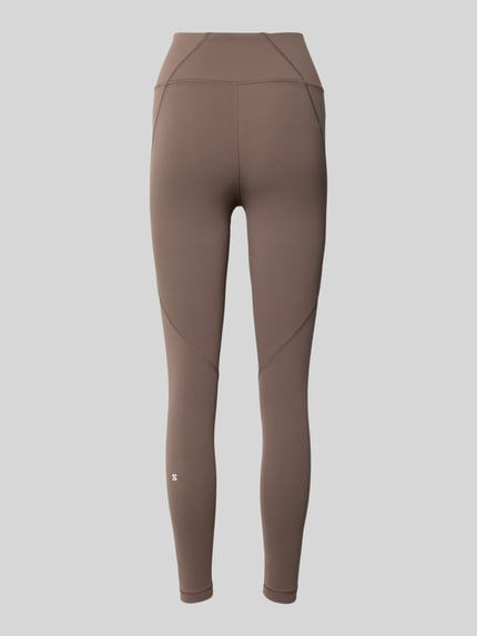 Vrouwenmodel draagt Leggings met Stretch-Anteil Modell 'SHKOUT' van Salomon in elastische, bruine stof, aansluitende fit, elastische tailleband, volledige lichaamsweergave achteraan.