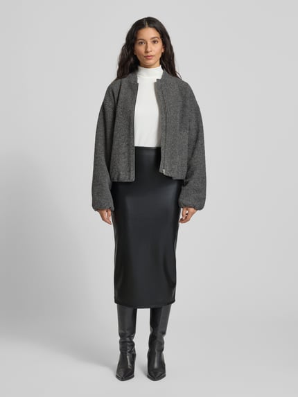 Frauenmodel trägt Midirock in Leder-Optik von ZABAIONE in Schwarz, körpernahe Passform, kombiniert mit grauer Jacke, Ganzkörperansicht von vorne.
