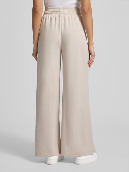 Frauenmodel trägt Wide Fit Stoffhose mit gelegten Falten von Christian Berg Woman in Beige, elastischer Bund, Material-Mix, Ganzkörperansicht Rückansicht.
