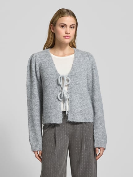 Kobiece model prezentuje szarą Strickjacke mit Schnürverschluss Modell 'GRSLULU' von FREE/QUENT, luźny krój, dzianina z dodatkiem wełny, V-dekolt, prążkowane wykończenia, przód zawiązywany, widok całej sylwetki od przodu.