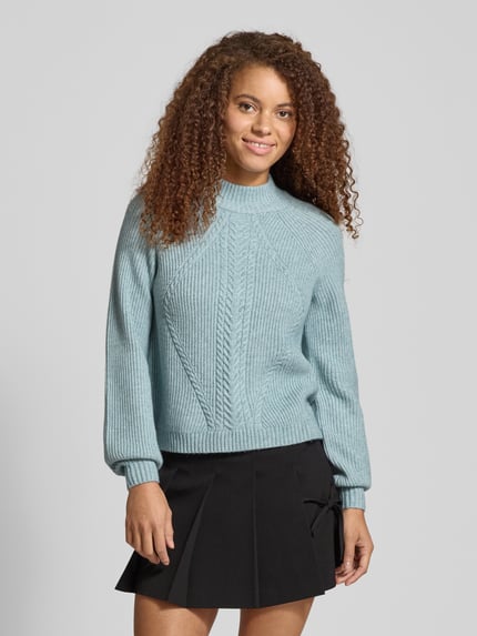 Kobiece modelka nosi Regular Fit Strickpullover aus Viskose-Mix Modell 'KATIA' od Only w kolorze melanżowym, wzór warkoczowy, ściągacze, widok całej sylwetki z przodu.