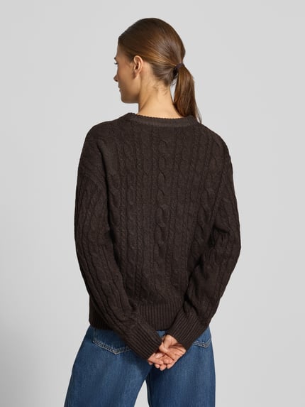 Frauenmodel trägt Pullover mit Zopfmuster Modell 'VMSEQUOIA' von VERO MODA, braun, Strick, gerippte Abschlüsse, Ganzkörperansicht Rückansicht.