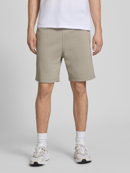 Männermodel trägt Shorts mit Label-Stitching mit elastischem Bund von CHAMPION in Beige, Regular Fit, Baumwoll-Mix, Ganzkörperansicht von vorne.