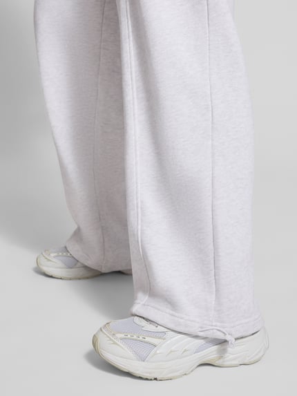 Frauenmodel trägt Oversized Sweathose aus reiner Baumwolle von PUMA, hellgrau, lässige Passform, grobe Textur, Nahaufnahme Beine.