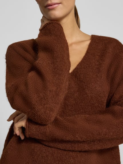 Frauenmodel trägt Relaxed Fit Strickpullover aus Alpaka-Mix Modell 'SOMAIJA' von DRYKORN in warmem Braun, V-Ausschnitt, Rollsaum, Nahaufnahme Oberkörper.