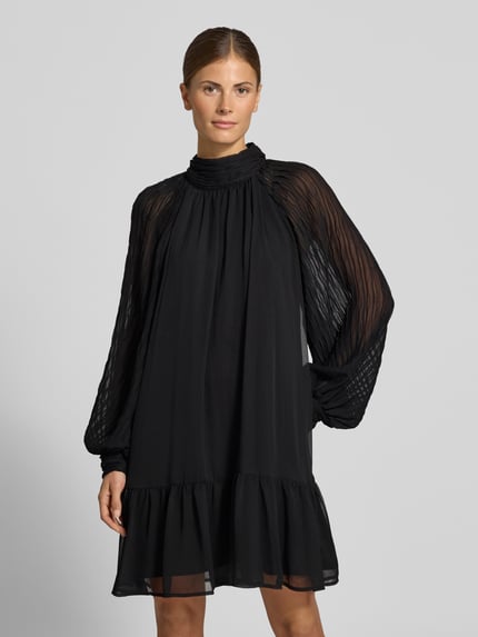 Frauenmodel trägt Minikleid mit Stehkragen Modell 'OLERA' von YAS in Schwarz, fließender Stoff, A-Linie, Ganzkörperansicht von vorne.