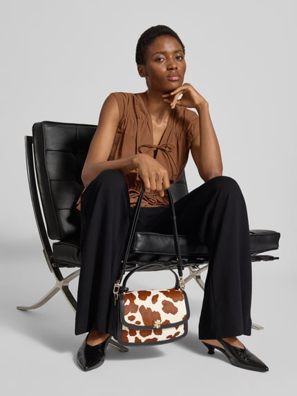 Frauenmodel trägt Crossbody Bag aus echtem Rindsleder Modell 'Audrey' von GUESS in Animal-Optik, Ganzkörperansicht von vorne. Hauptfach mit Überschlag, abnehmbarer Schulterriemen, Magnetverschluss, Logo-Detail, Maße 24x16x9 cm, Länge Schulterriemen 82 cm.