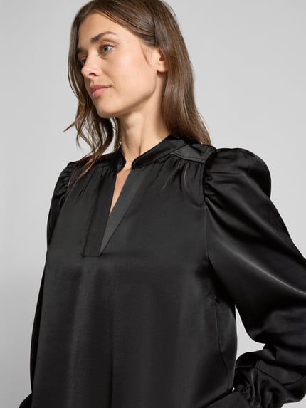 Vrouwenmodel draagt Langarmbluse met Stretch-Anteil Modell 'Rosslyn' van Neo Noir, zwarte satijn, V-hals, ballonmouwen, detailopname bovenlichaam.