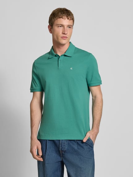Männermodel trägt Straight Fit Poloshirt mit Label-Stitching von Calvin Klein Jeans in Grün, reine Baumwolle, Ganzkörperansicht von vorne.