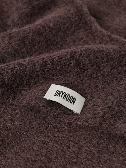 Produktfoto, Dreieckstuch mit Woll-Anteil von DRYKORN in Braun, Strick-Optik, weiche Textur, Label-Patch, Detailaufnahme. Material-Mix, eingefasste Abschlüsse, Breite bei Größe 1: 58 cm.