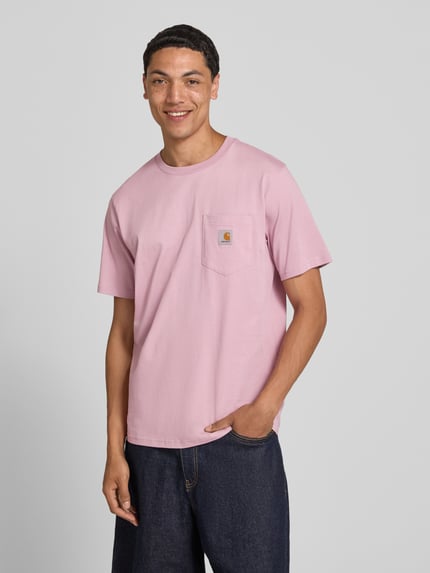 Männermodel trägt Regular Fit T-Shirt mit Brusttasche von Carhartt Work In Progress in Rosa, Reine Baumwolle, Label-Patch, Ganzkörperansicht von vorne. Herren T-Shirt mit Rundhalsausschnitt, Rückenlänge bei Größe M 71 cm.