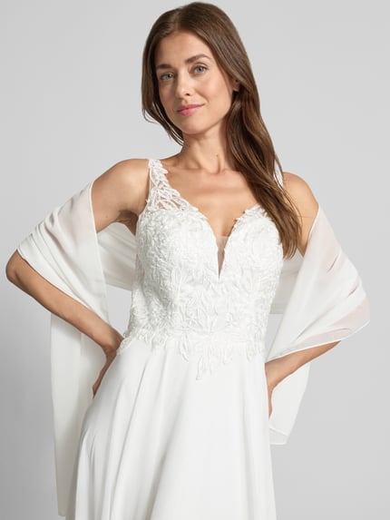 Frauenmodel trägt Abendkleid mit Spitze und tiefem V-Ausschnitt von Mascara, Weiß, Chiffon, A-Linie, Detailaufnahme Oberkörper. Damen Abendkleid von Mascara, Maxikleid, tiefer V-Ausschnitt, Spitzenbesatz, Rückseite mit Haken- und Reißverschluss, Rückenlänge 155 cm, Brustweite 39 cm.