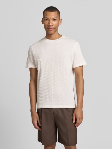 Männermodel trägt T-Shirt mit Strukturmuster Modell 'Raulos' von JOOP! Collection aus reiner Baumwolle, Modern Fit, Rundhalsausschnitt, Label-Detail, Vorderansicht Nahaufnahme Oberkörper.