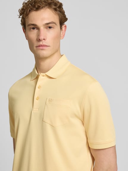 Männermodel trägt Regular Fit Poloshirt mit Brusttasche und Label-Stitching von bugatti in Hellgelb, glatte Textur, Nahaufnahme Oberkörper.